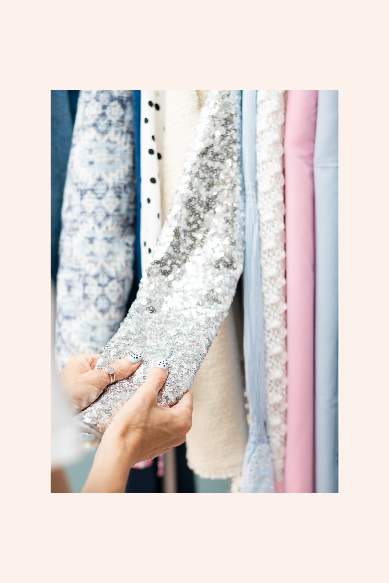Person holding a silver, sparkling, sequined fabric next to a row of various colorful fabrics on a clothing rack.