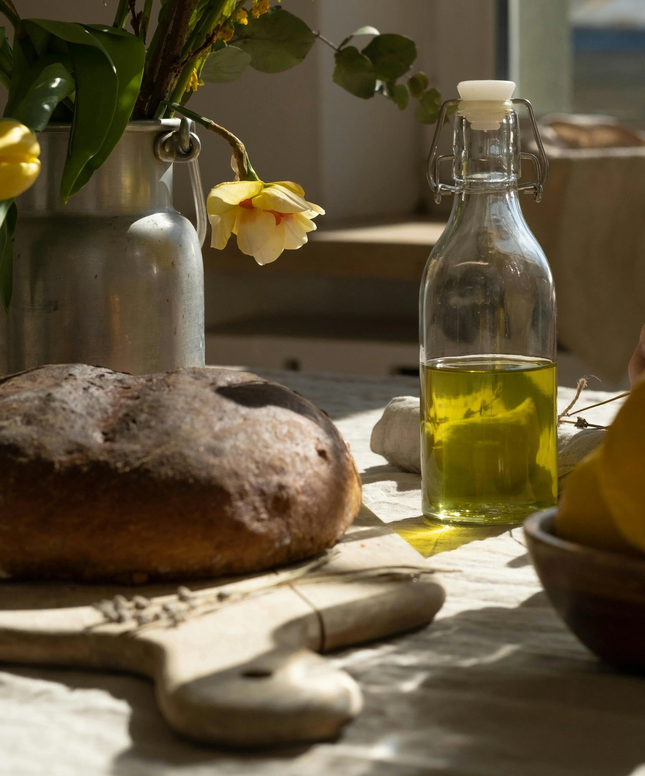 a loaf of sourdough on a table with a bottle of olive oil and flowers