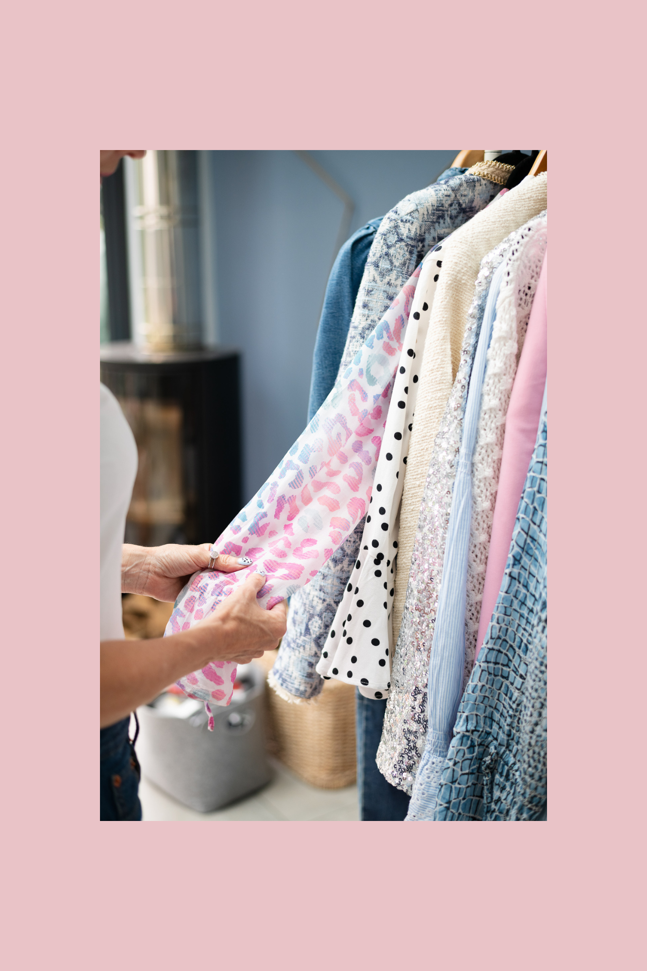 Person shopping for colorful clothing on a rack with pink, white, black, blue, and patterned fabrics, holding a pink and white animal print scarf.