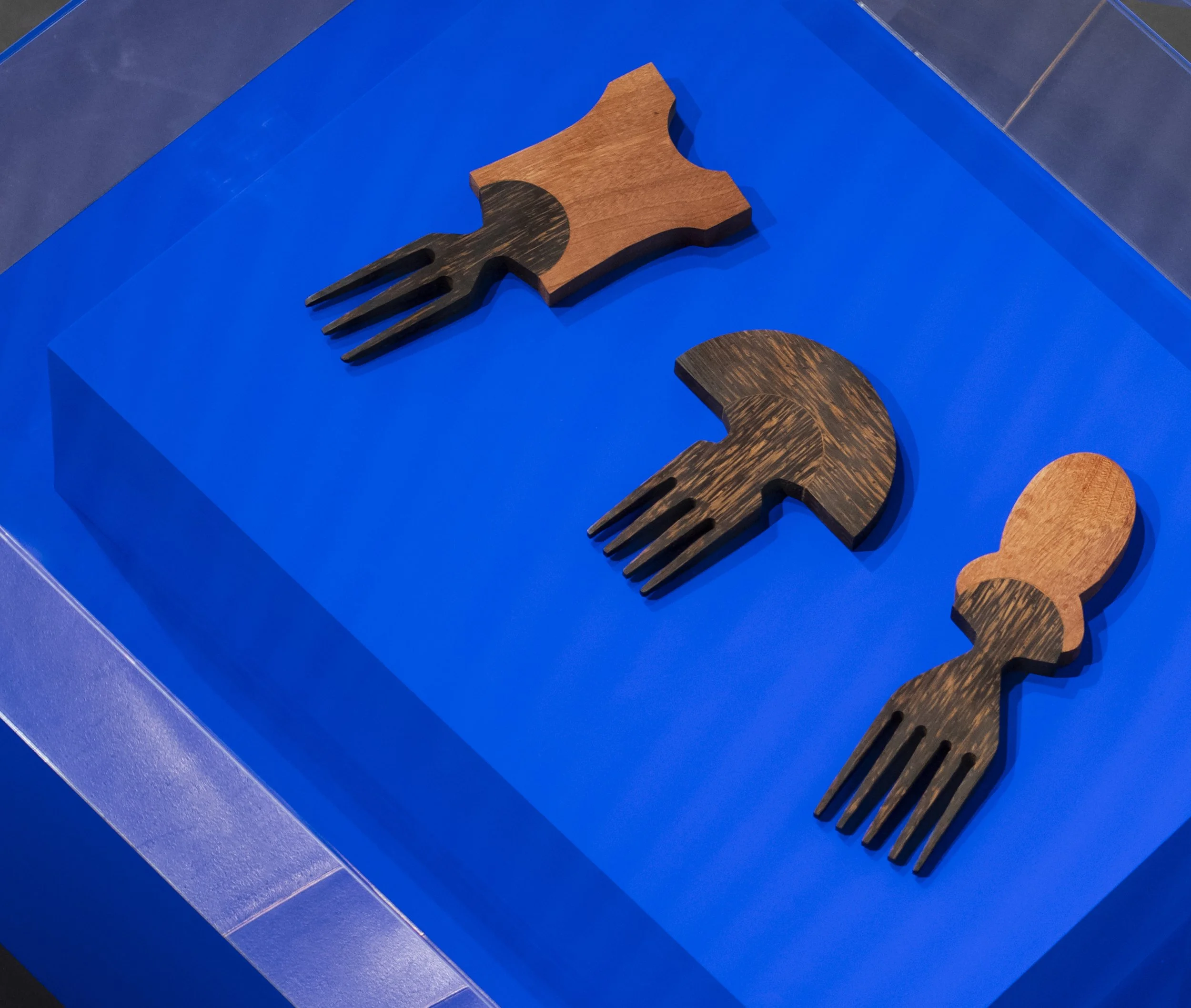 An overhead image of the three Crown combs, handcarved by Simone Brewster, sitting on a Klein blue table in The Shape of Things exhbition at the NOW Gallery. The Crowns collection is made up of sculptural combs, inspired by African hairstyles
