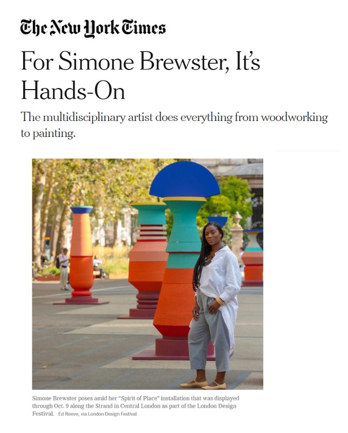 Photograph of Simone Brewster standing outdoors among colorful sculptural installations, with trees and a few people in the background. Article  in The New York Times on artist Simone Brewster  and her public art installation in London.