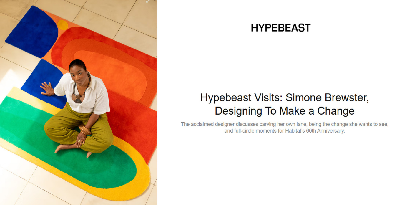 Artist Simone Brewster sitting on a colorful abstract rug with geometric shapes in red, blue, green, and yellow, looking up at the camera. Photo for HYPEBEAST magazine feature. Article that discusses Brewster's design work with Habitat.