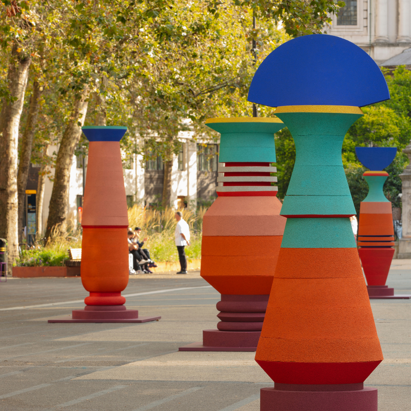 Colorful abstract art sculptures in a city park with trees and buildings in the background. Public art installation by Simone Brewster, 'Spirit of Place'.
