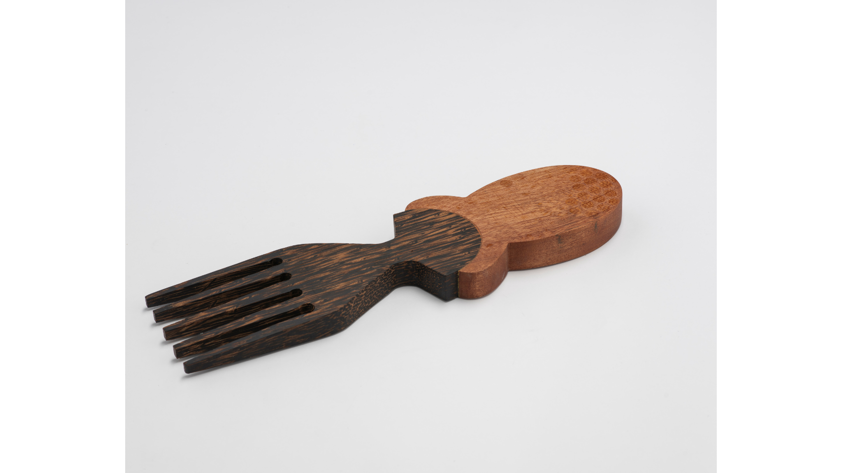 Five prong comb laid flat on white surface hand-carved from black palm wood with accents of sapele. The comb draws on the distinctive hairstyles of specific African communities
