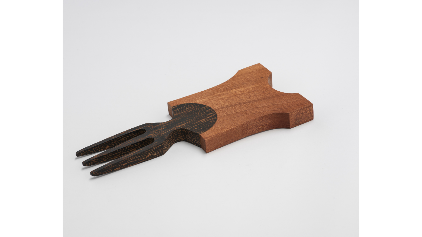 Three prong comb laid flat on white surface hand-carved from black palm wood with accents of sapele. The comb draws on the distinctive hairstyles of specific African communities