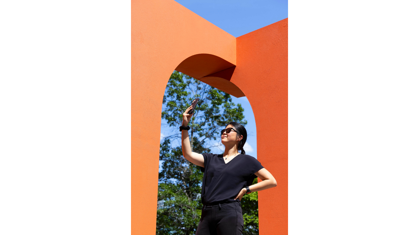A woman stands in the corner archway of the Temple of Relics public installation by Simone Brewster. The lady is taking a photograph