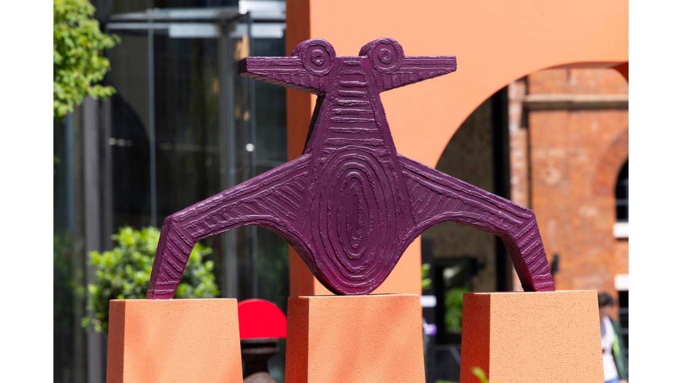 Close up image of a purple sculpture that rests upon three angular pillars.