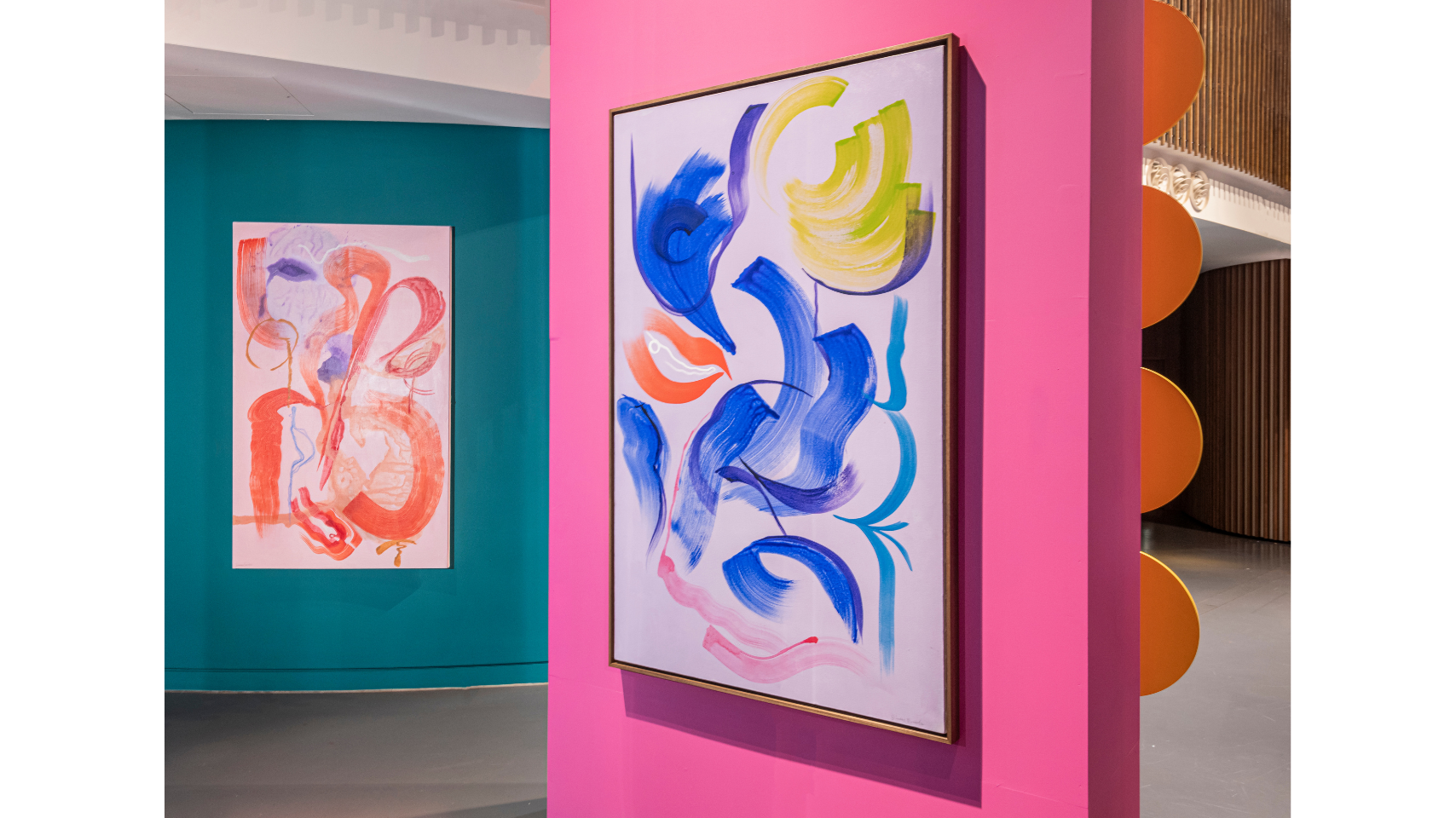 Inside the exhibition space, two colourful paintings by Simone Brewster, one in the foreground and one in the background both hang on brightly coloured walls