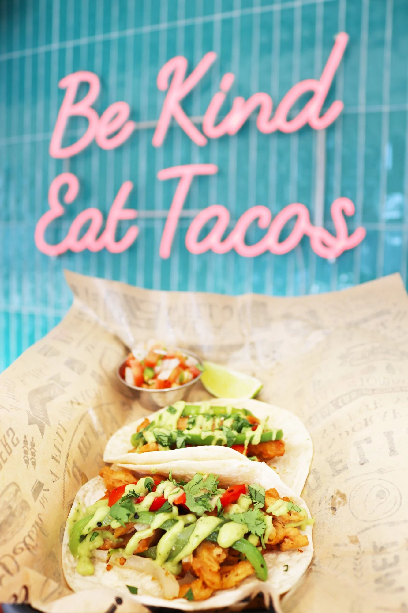 vegan tacos with a neon sign in the background that reads' Be Kind Eat Tacos"