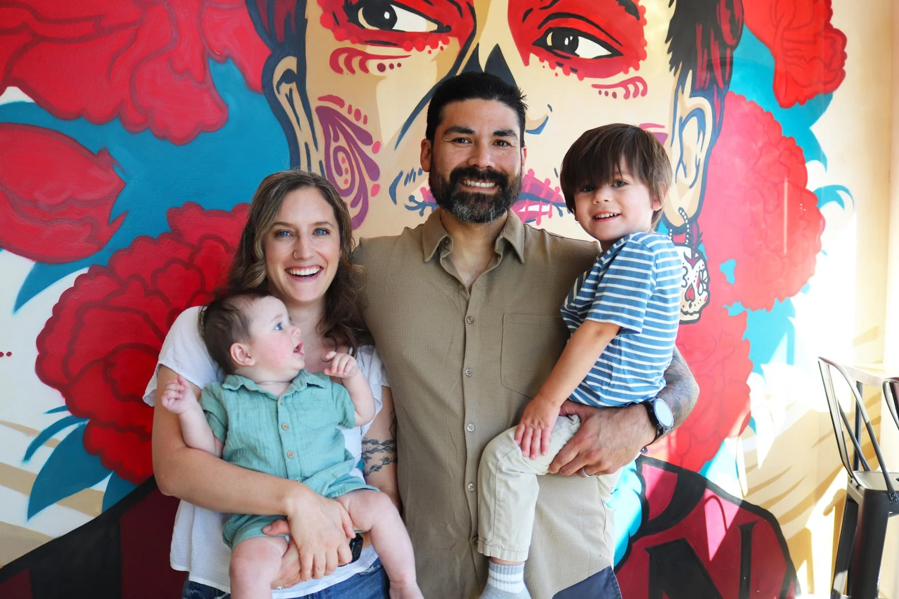 Milton and Rachel, owners of Taco Vegana, with their children in front of an interior mural of Frida Kahlo
