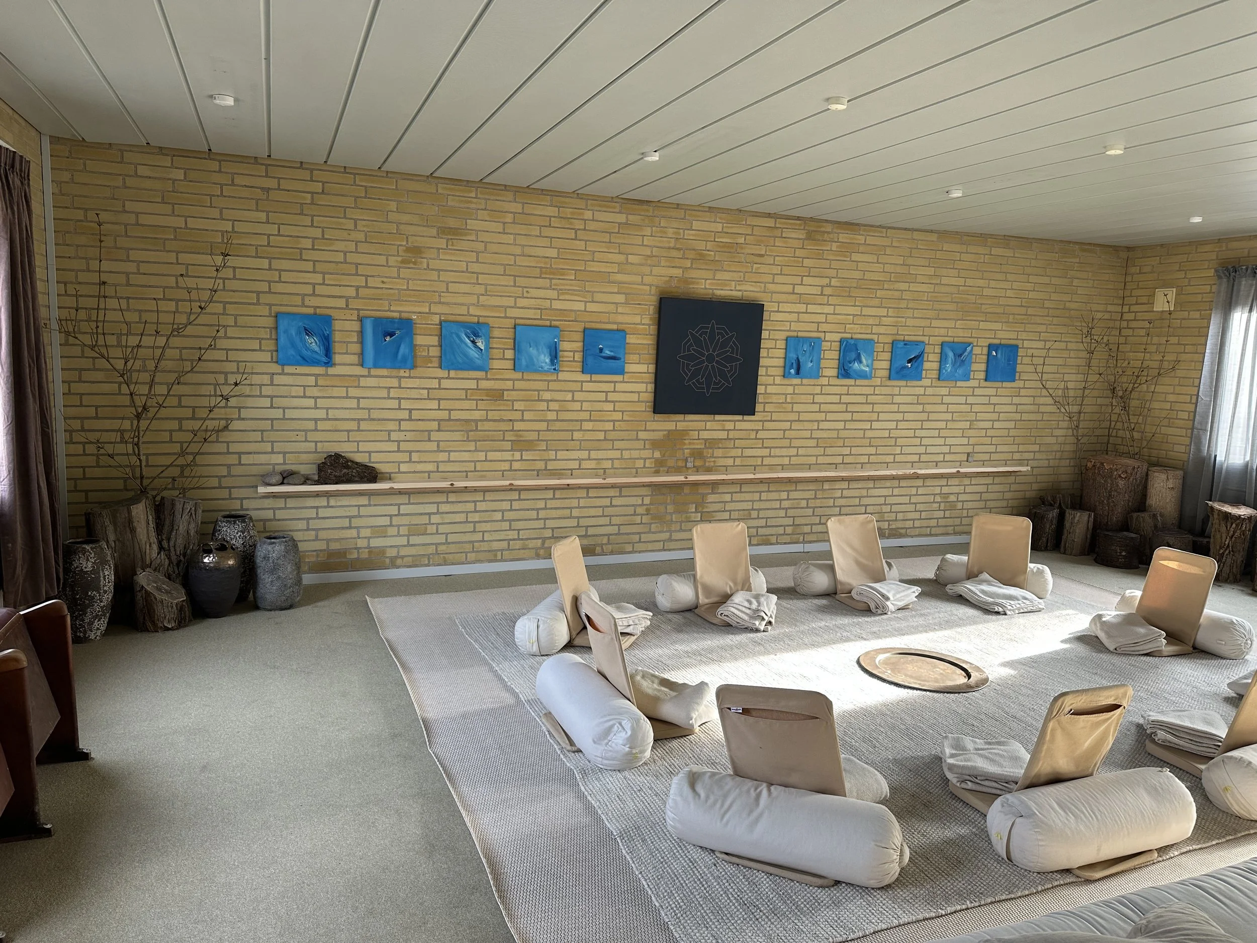 Indendørsræsscene med beige stole, foldede håndklæder, tæpper, store stenskulpturer og vægkunst i en hyggelig atmosfære.