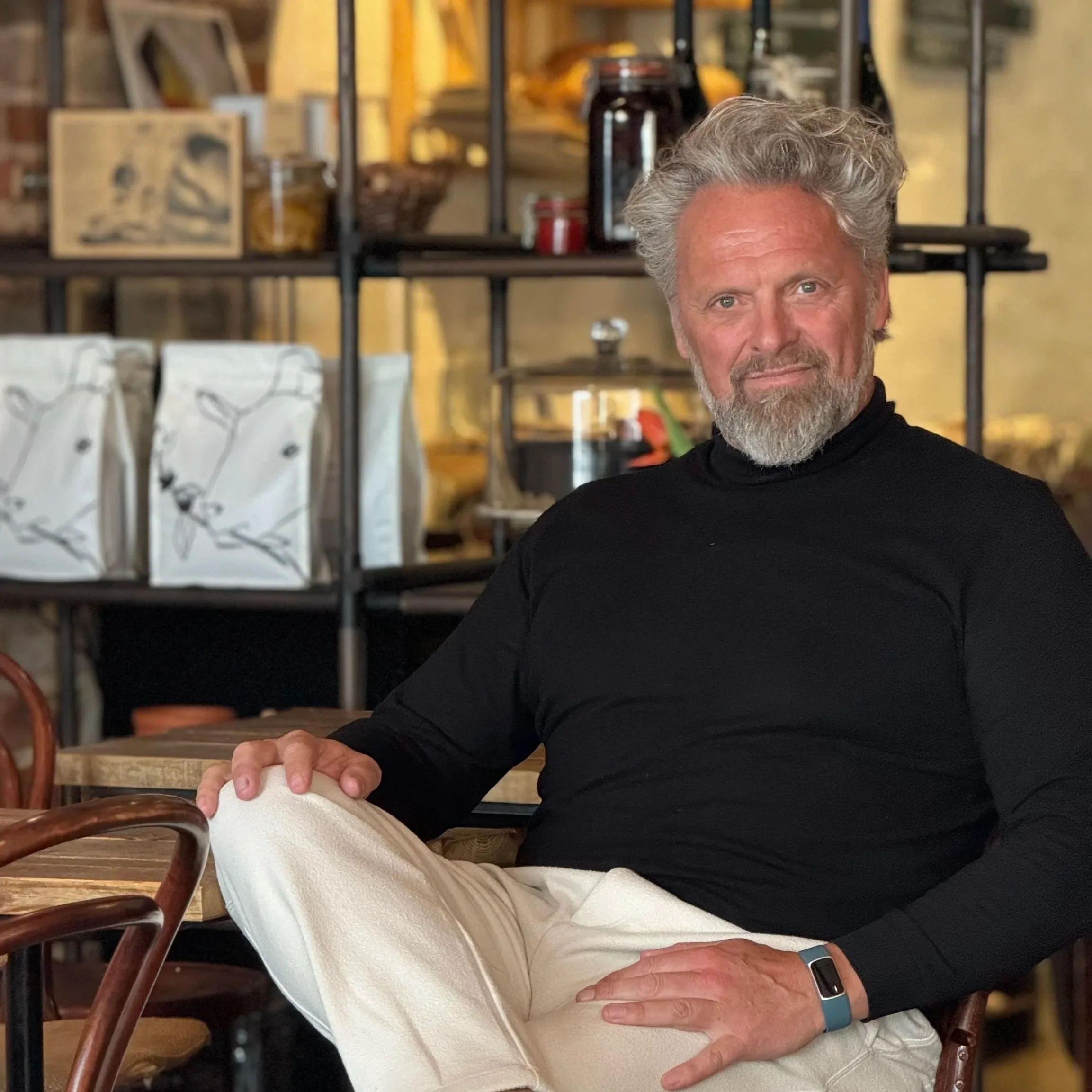 Et ældre par sidder sammen i en restaurant. Kvinden har blond hår og bærer hvid bukser, mens manden har gråt hår og skæg, og bærer en sort sweater.