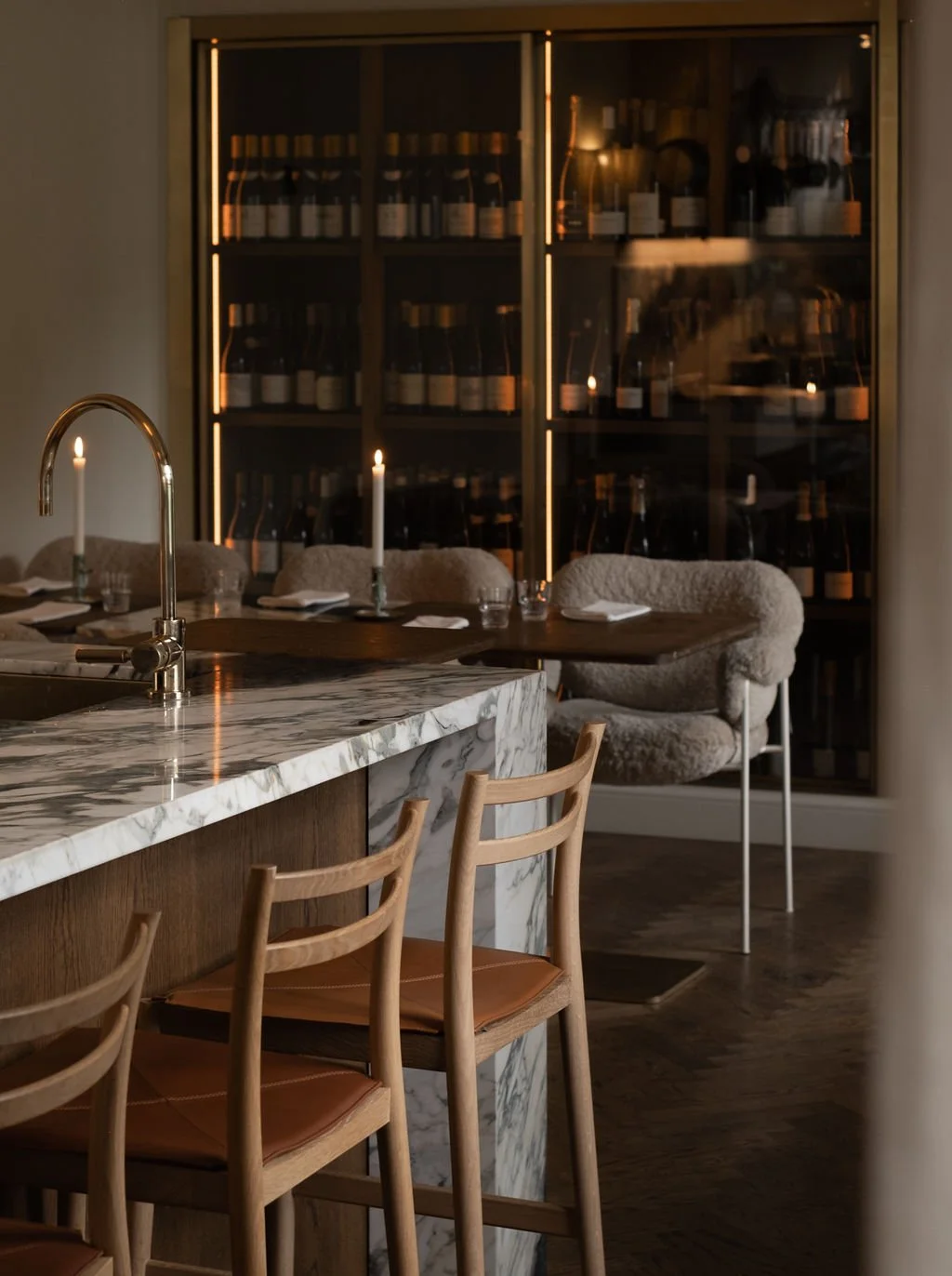 Interiør av en koselig restaurant med stearinlys, barstoler, og en vinlagringshylle i bakgrunnen.