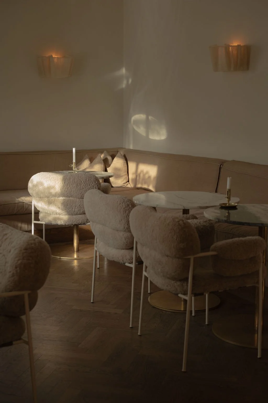 Elegant stue med beige sofa, rundt bord med lys, myke puter, og moderne lysskulpturer på veggen