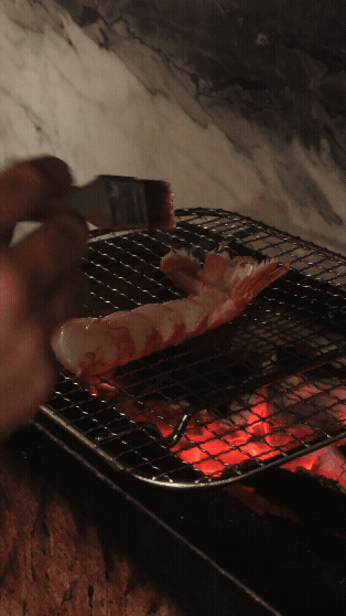 Sjømat, sannsynligvis en reke, grilles på grill over kull.