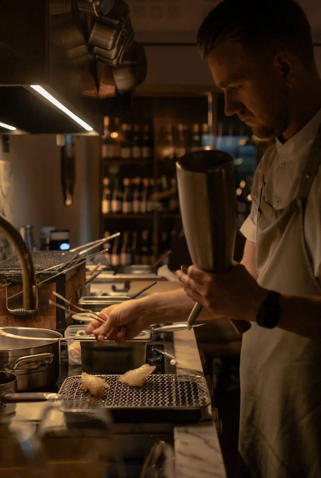 En kok i en restaurant som tilbereder mat på en komfyr i et kjøkken med mørk belysning.