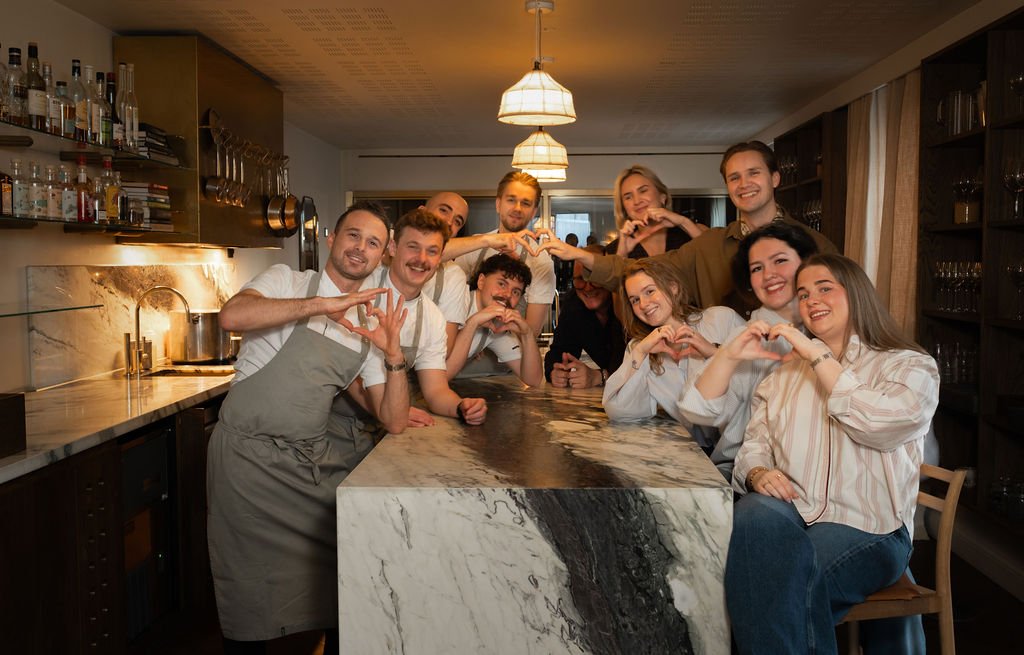 En gruppe mennesker i en restaurant eller bar viser hjerteformer med sine hender.