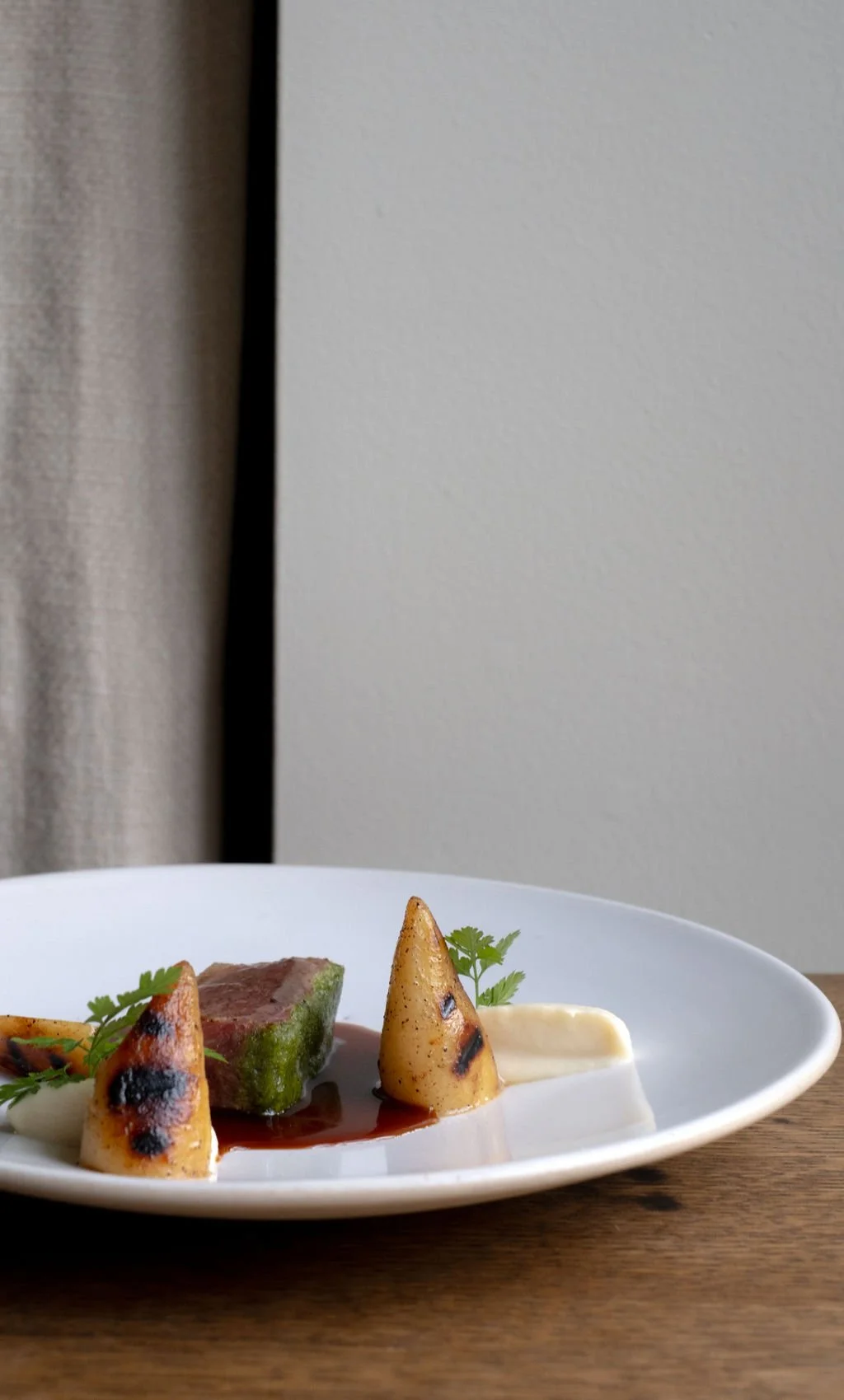 Stek med poteter, rød saus, urter og potetstykker servert på en hvit tallerken.