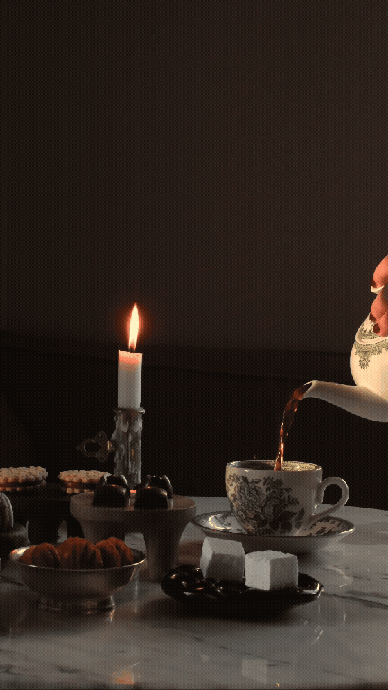 Kaffeekopp med te som blir hellet i. Telyslykter, kjeks, sjokolade, og marshmallows på bordet.