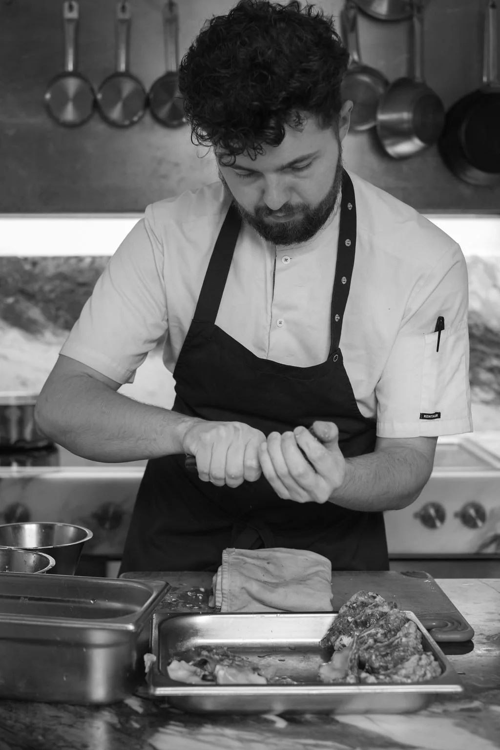 Kokk som forbereder mat i et kjøkken, med kjøkkenutstyr og råvarer foran seg.