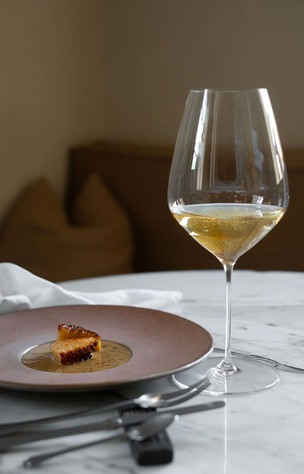 Et glass hvitvin og en tallerken med mat på et hvitt marmorbord.