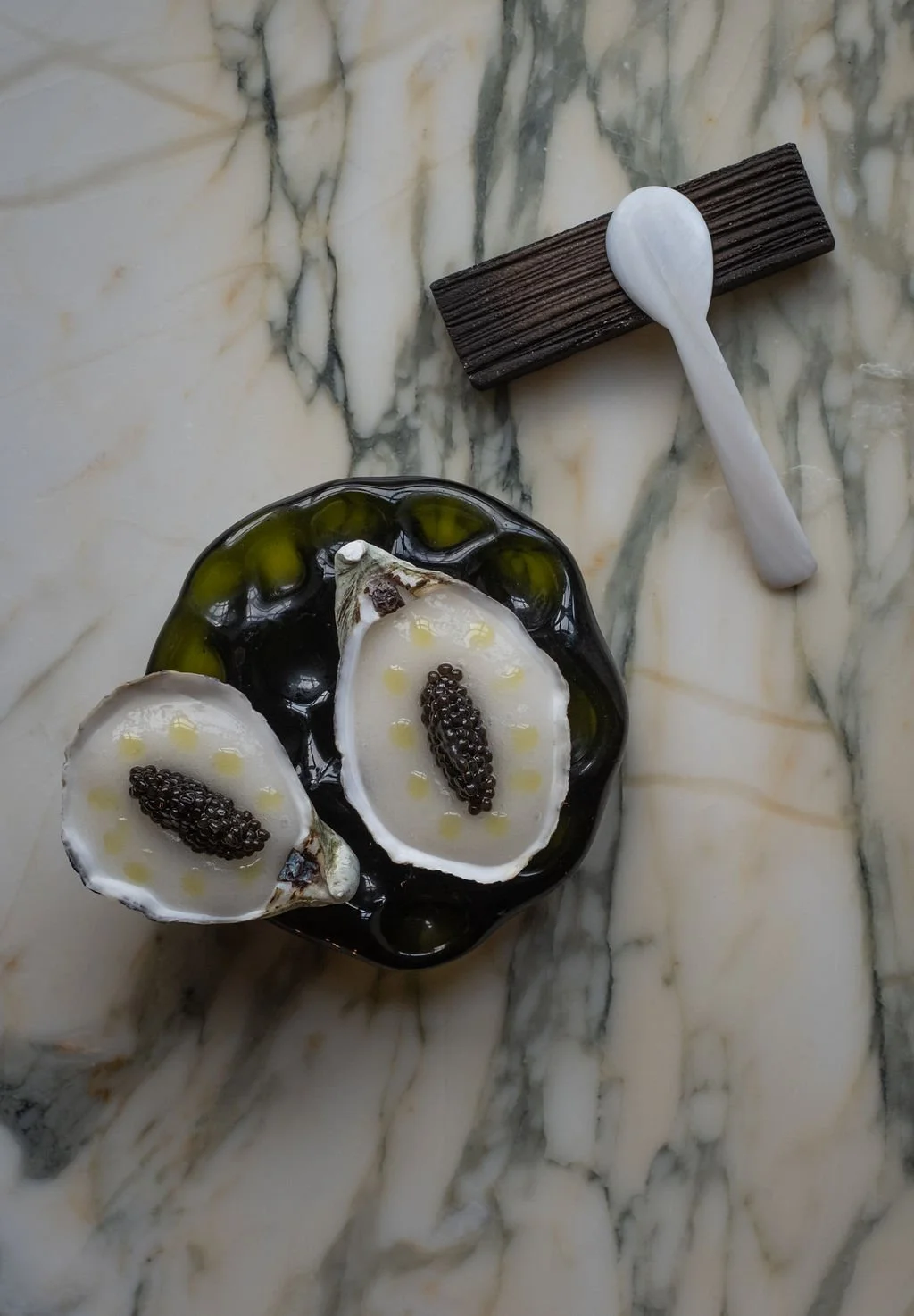 To åpne skjell fylt med en hvit krem og svarte kaviar, servert på en svart tallerken på en marmorgulv.