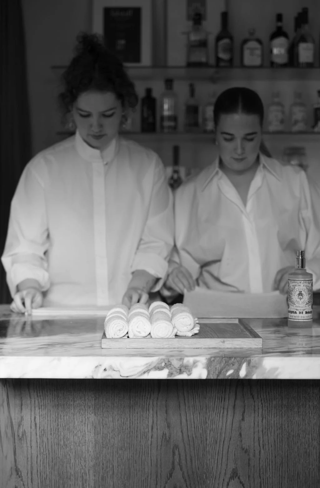 To kvinner står bak en bar med ruller med hvitt stoff eller håndklær på en treplate.