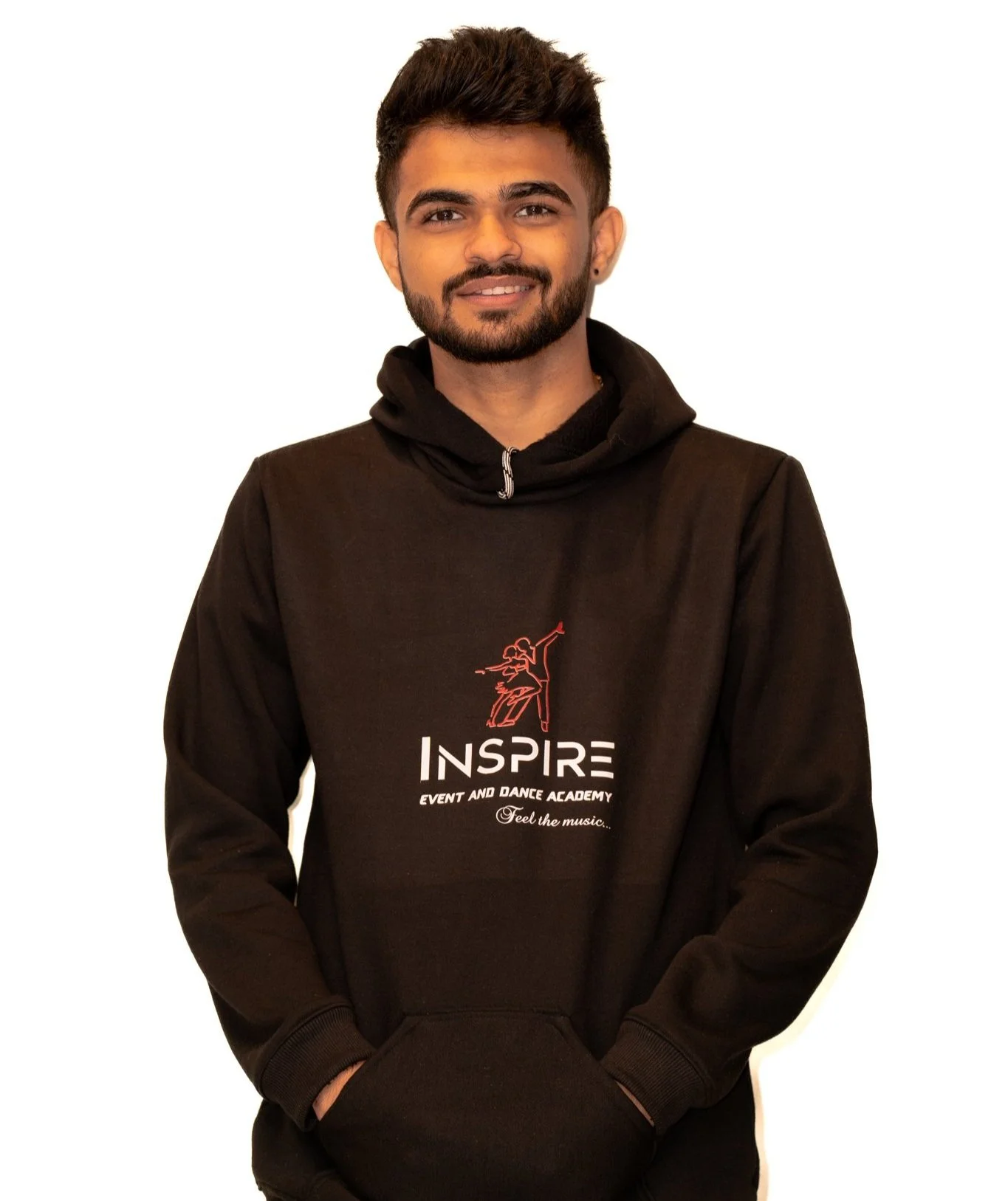 A young man with short dark hair, beard, and earrings, smiling, wearing a black hoodie with red and white text and graphics that say "INSPIRE Event and Dance Academy" against a white background.