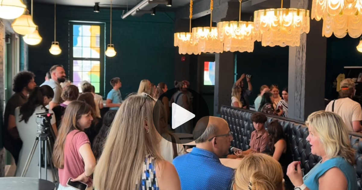 A crowd gathers for the grand opening of Swanky Scoops artisan ice cream shop in downtown Toledo Ohio. Crowd of people in line awaiting ice cream in a renovated Warehouse District building with turquoise walls, black leather booths, and chandeliers.