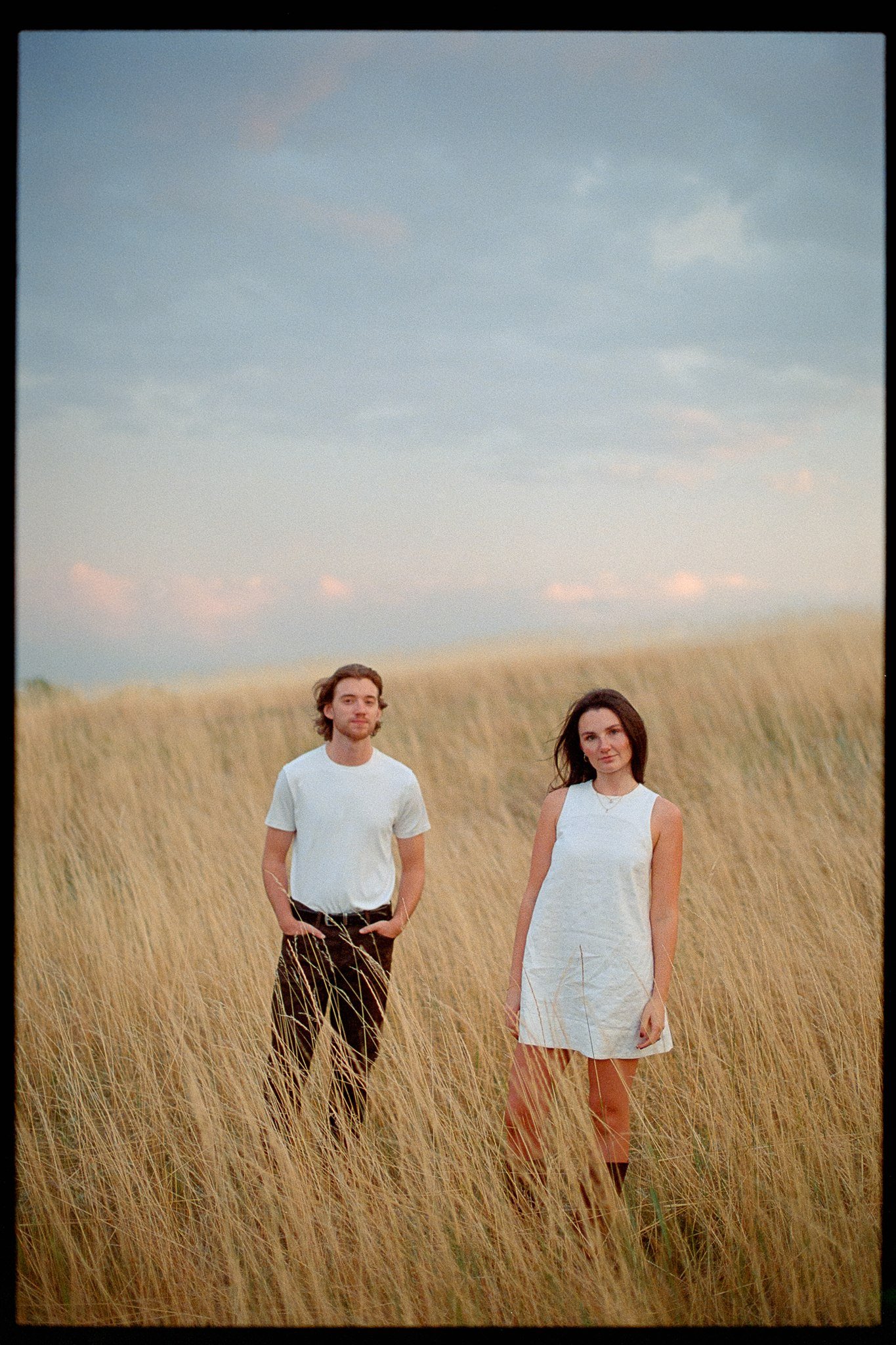 A man and woman standing in a grassy field with a cloudy sky in the background.