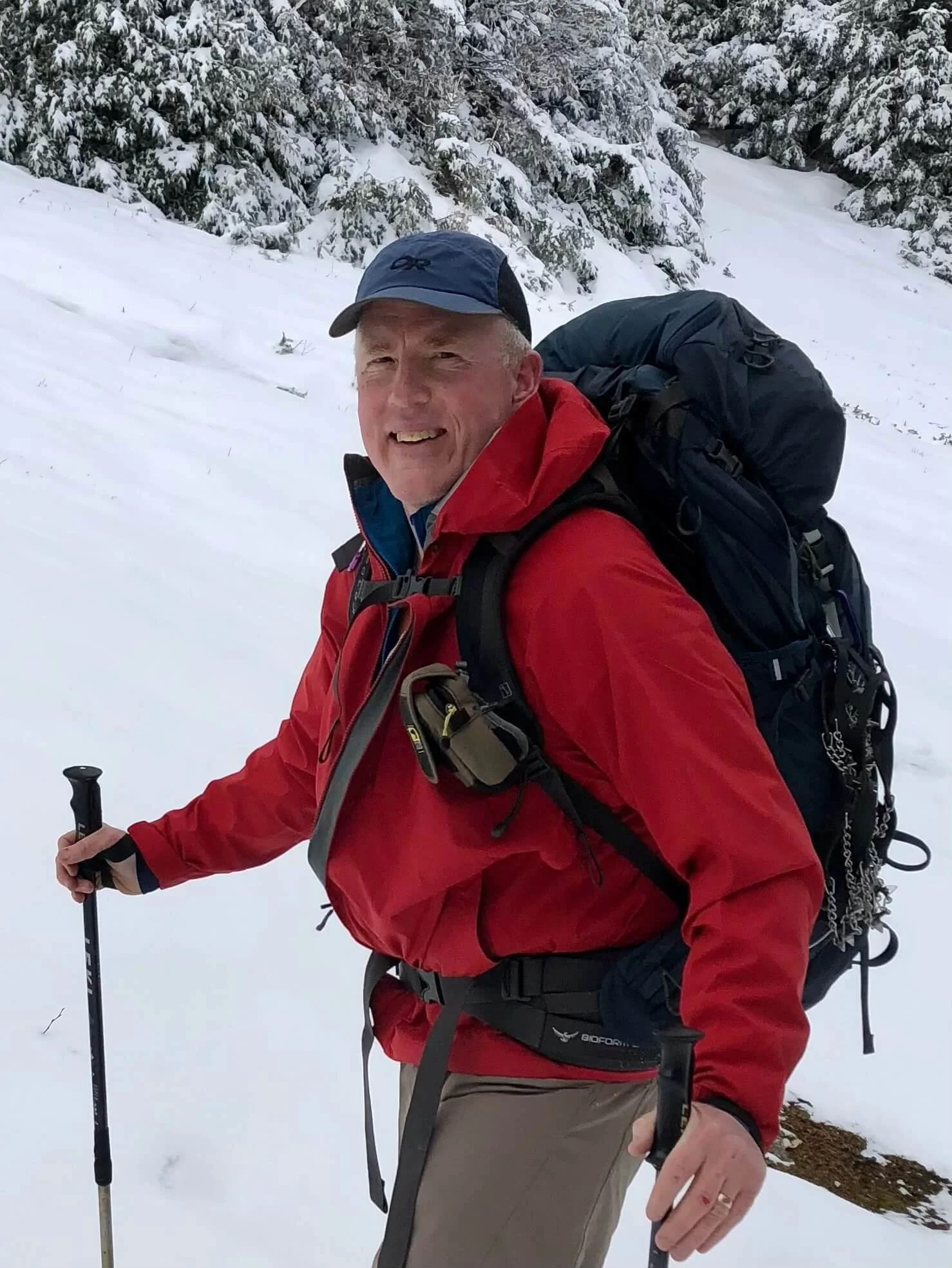 Brian Degen with a red jacket and ball cap hiking in the winter.