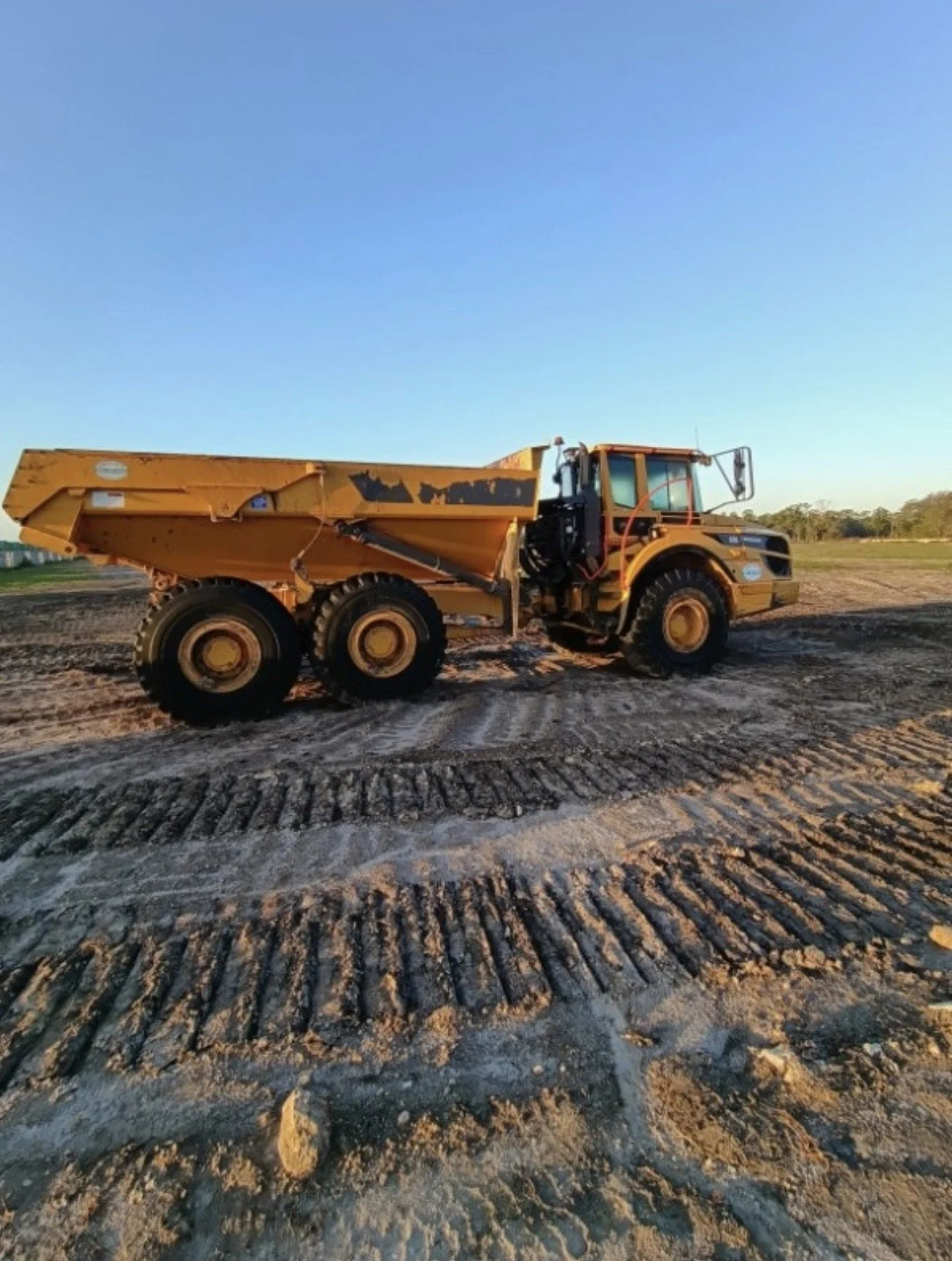 A large yellow construction dump truck on a dirt construction site during sunset.