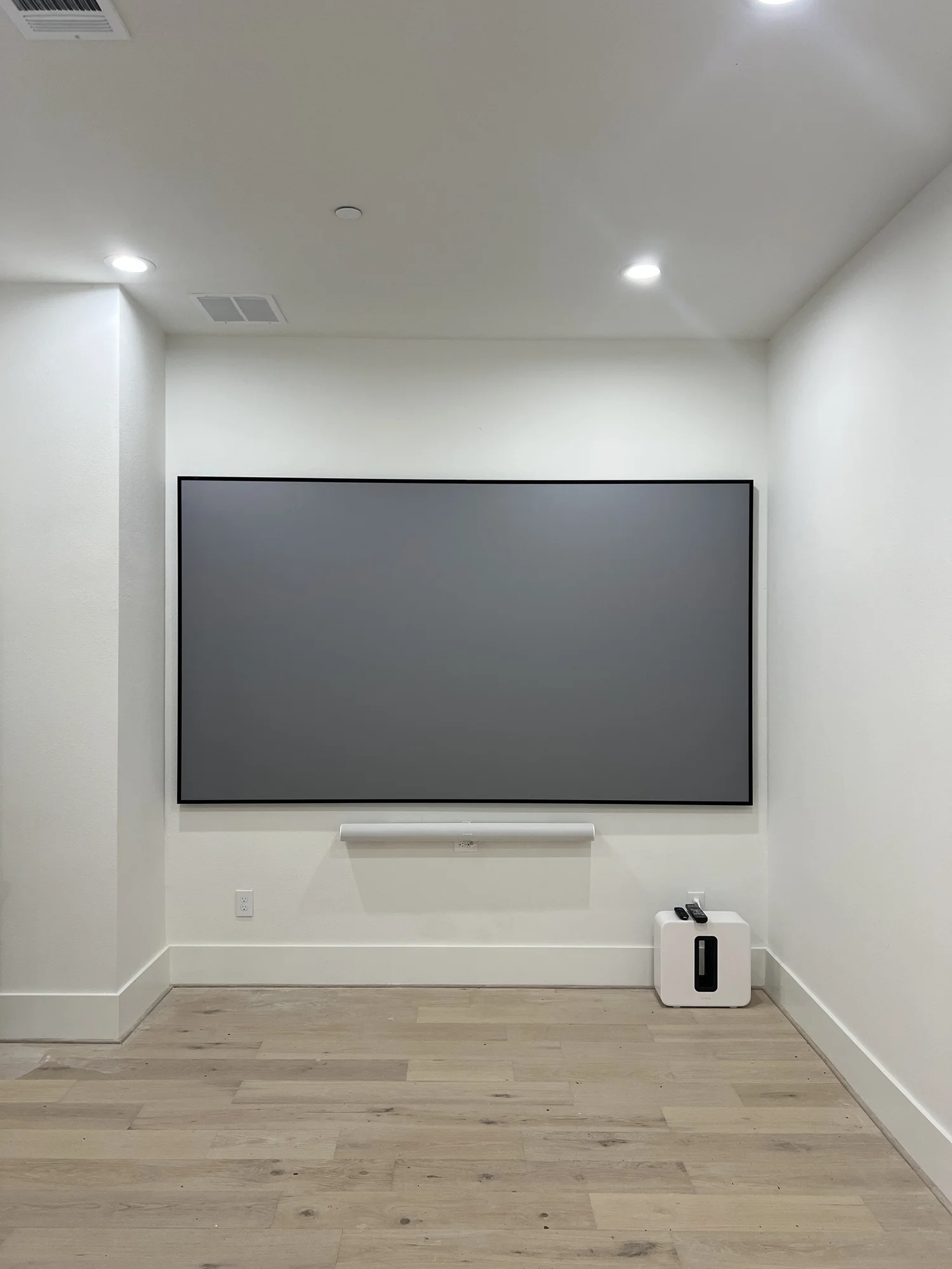 Projection screen with a white Sonos soundbar and subwoofer in a CLM installation