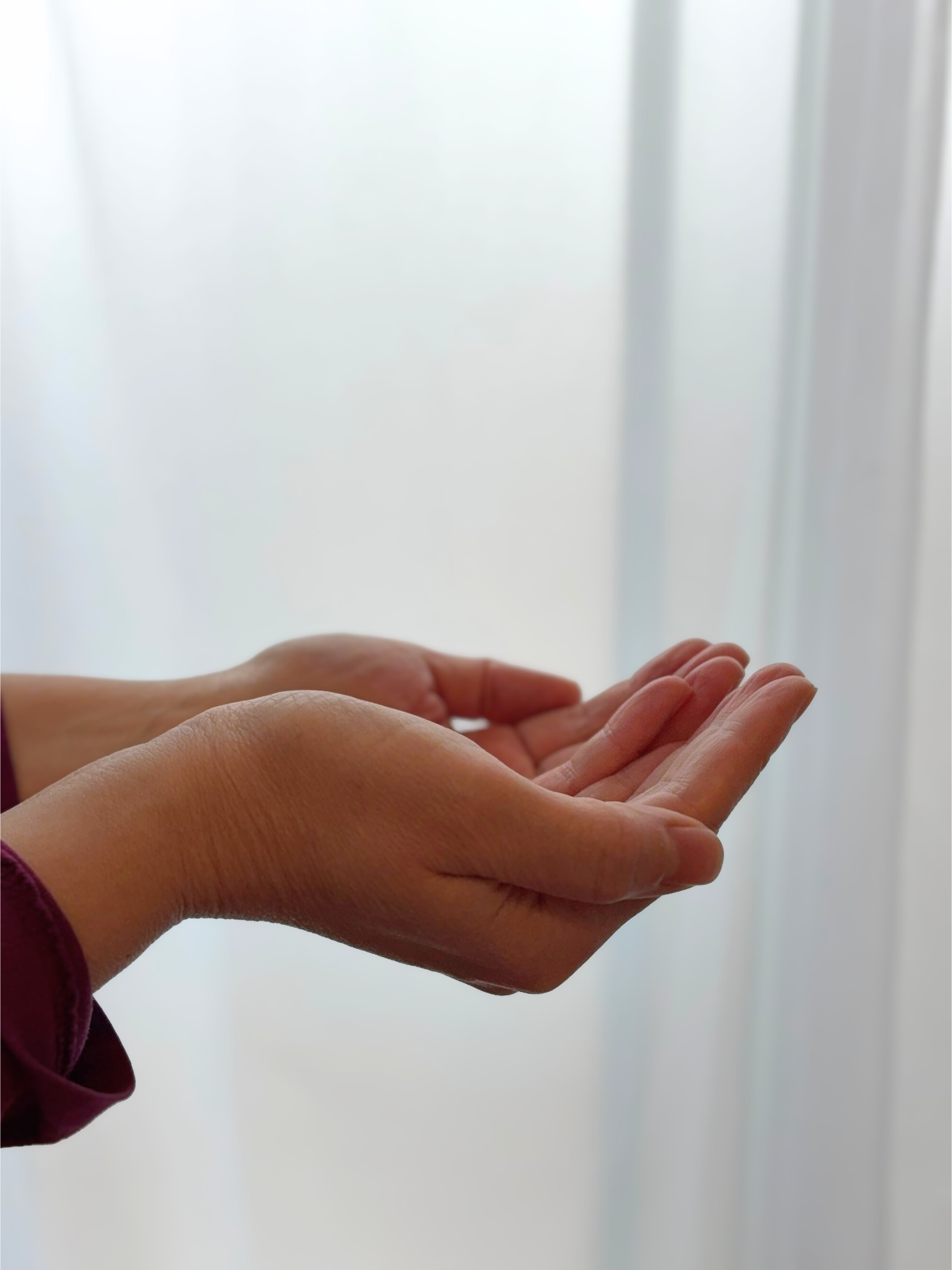 Two hands gently cupped together in front of sheer white fabric, conveying calm, presence, and care.