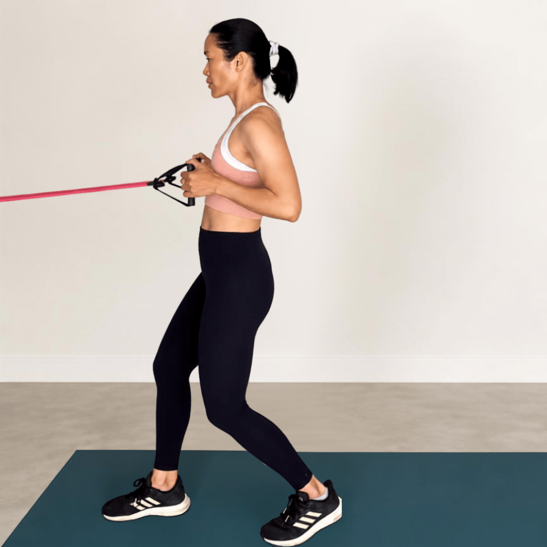 Woman using a resistance band on a mat, in a pink sports bra and black leggings, demonstrating upper-back strength.