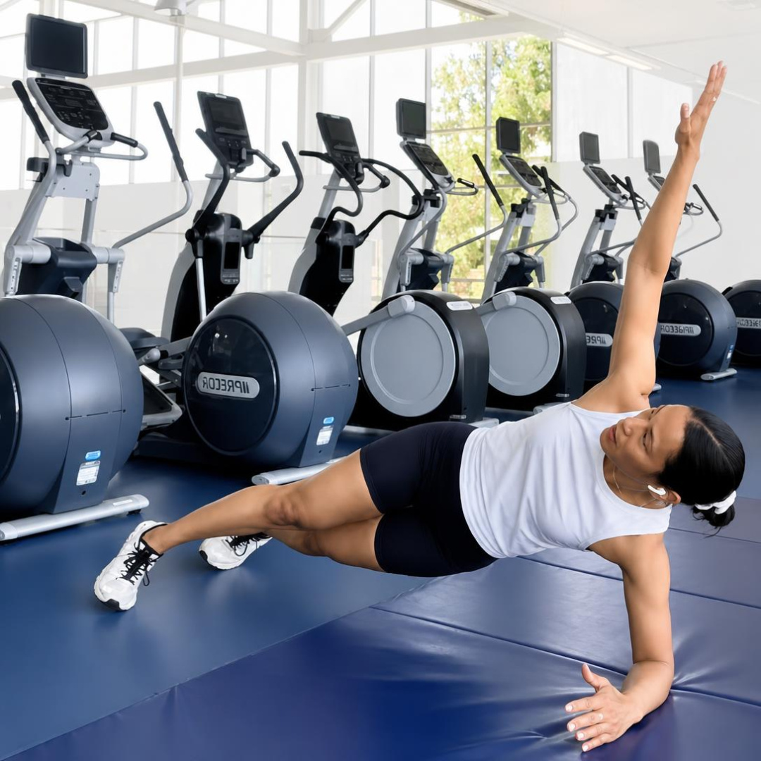 Person doing plank rotations on a blue mat in a gym, in a white top and black shorts, showing core strength and stability.