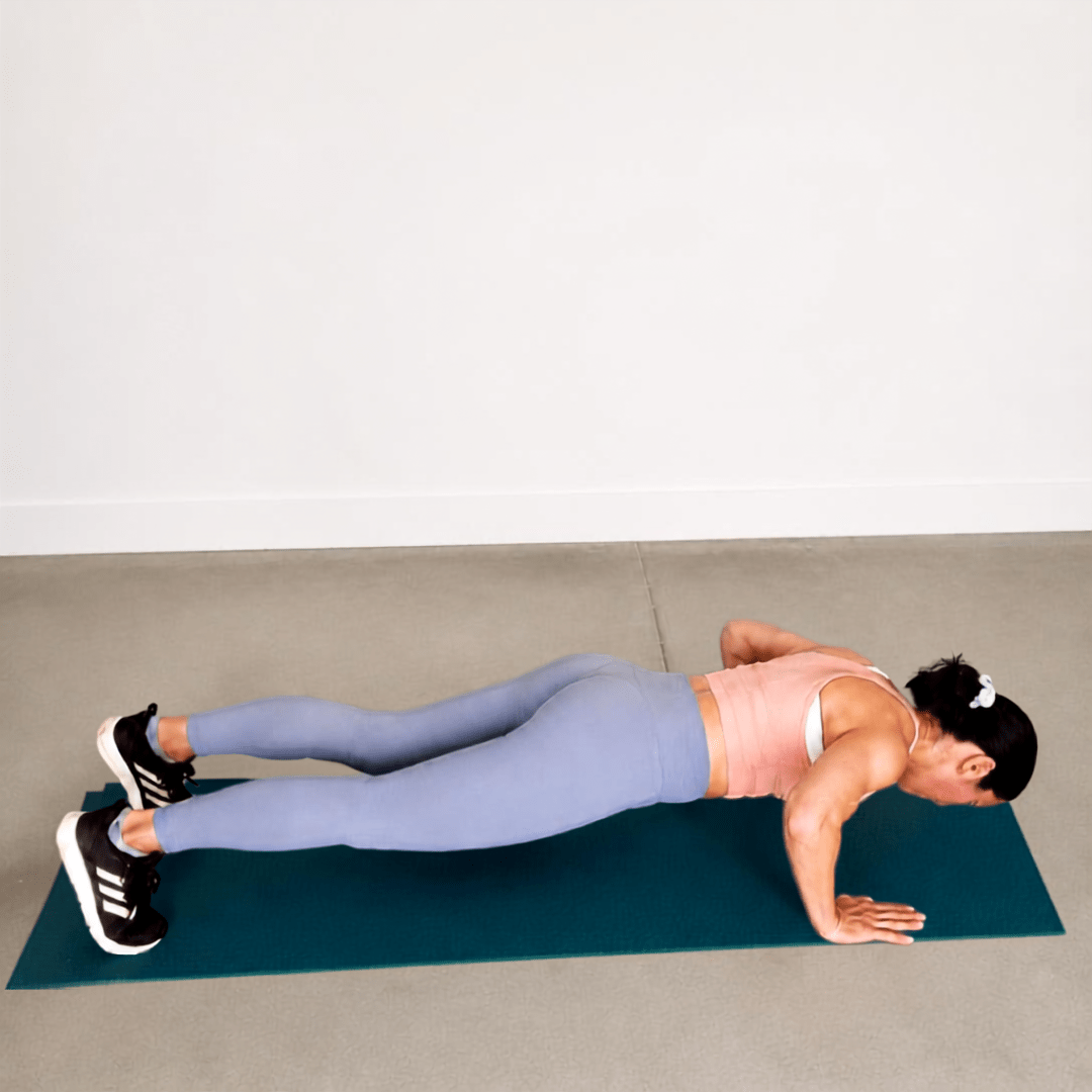 Woman doing a push-up on a teal mat, in a pink top and blue leggings, demonstrating chest, shoulder, and core strength.