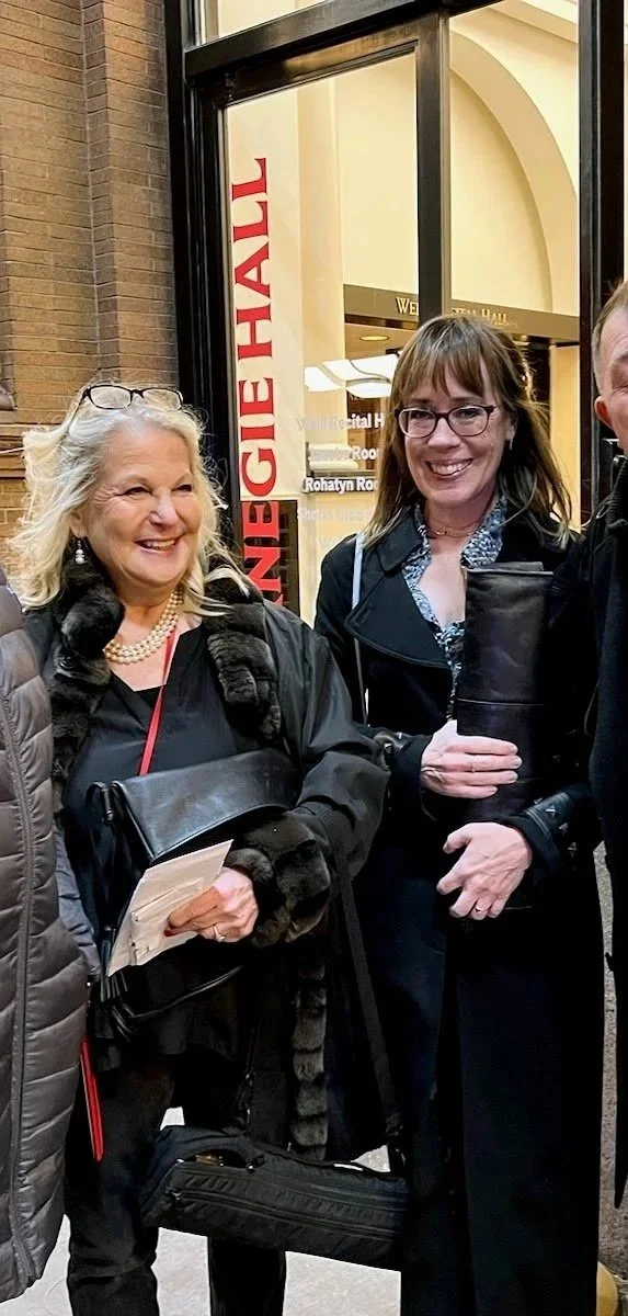 Three smiling people standing outside a hospital, with a sign for a regional hospital and a red sign reading 'Emergency Hall' visible behind them.