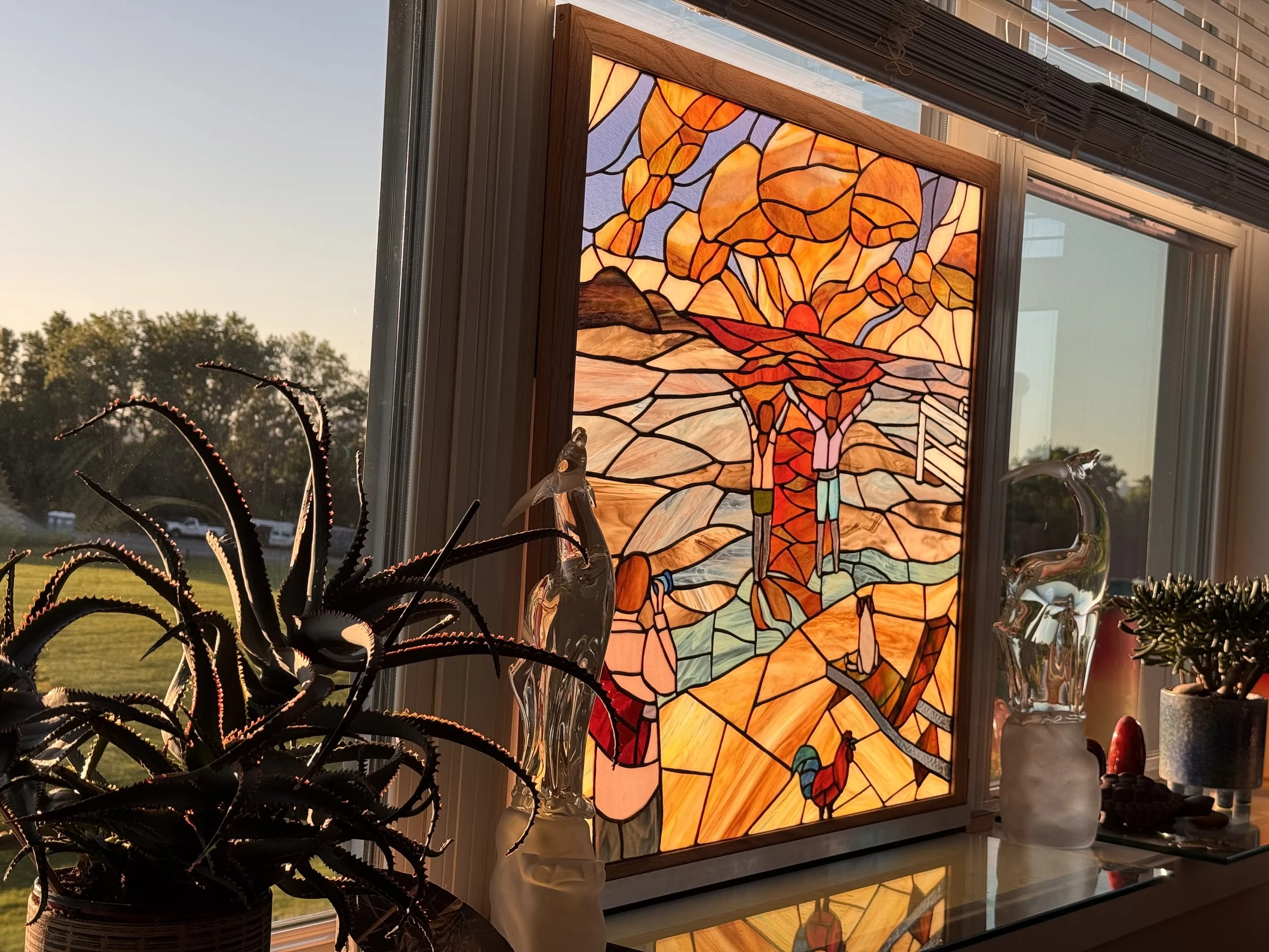 A stained glass window featuring a glowing sunrise featuring figures, photographer, dog on beach, rooster, illuminated by the sunlight
