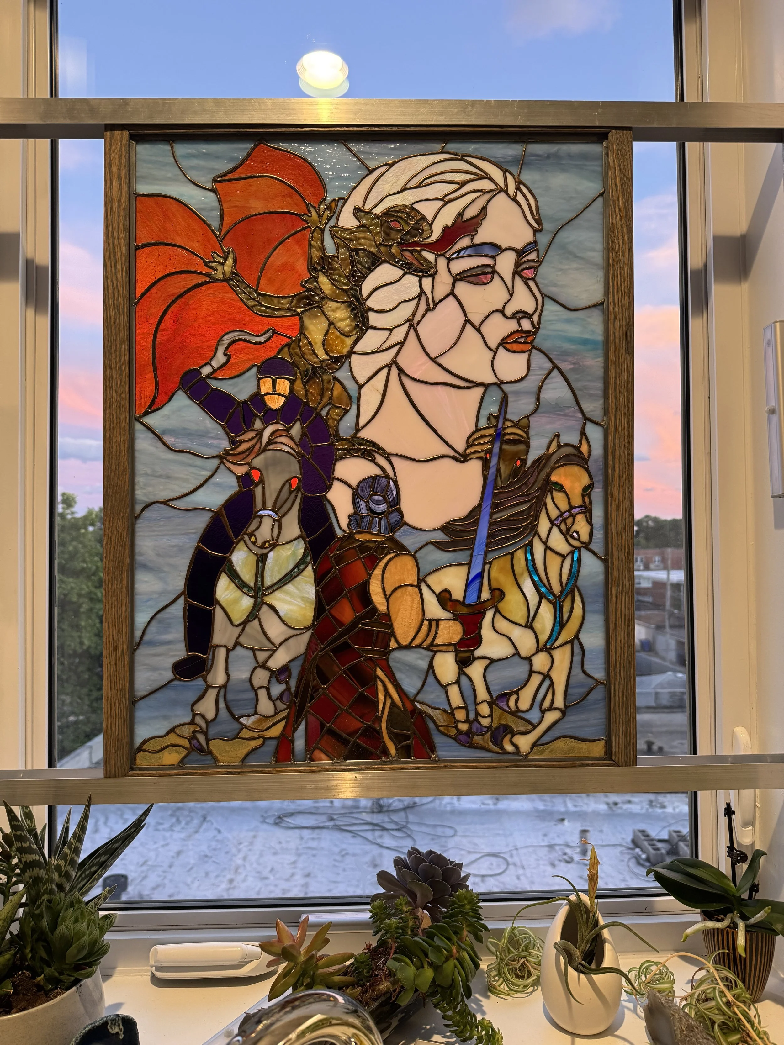 Stained glass window depicting a woman with long hair, a knight with a sword, a dragon, a horse, and a warrior, with a colorful background, framed by a wooden border, set against a window with a view of a snowy outdoor scene.