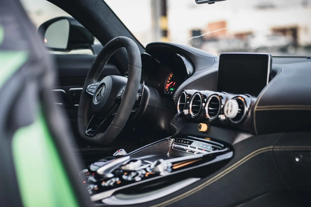 Wide open-door cabin view of the steering wheel, dashboard screen, round vents and yellow stitching.