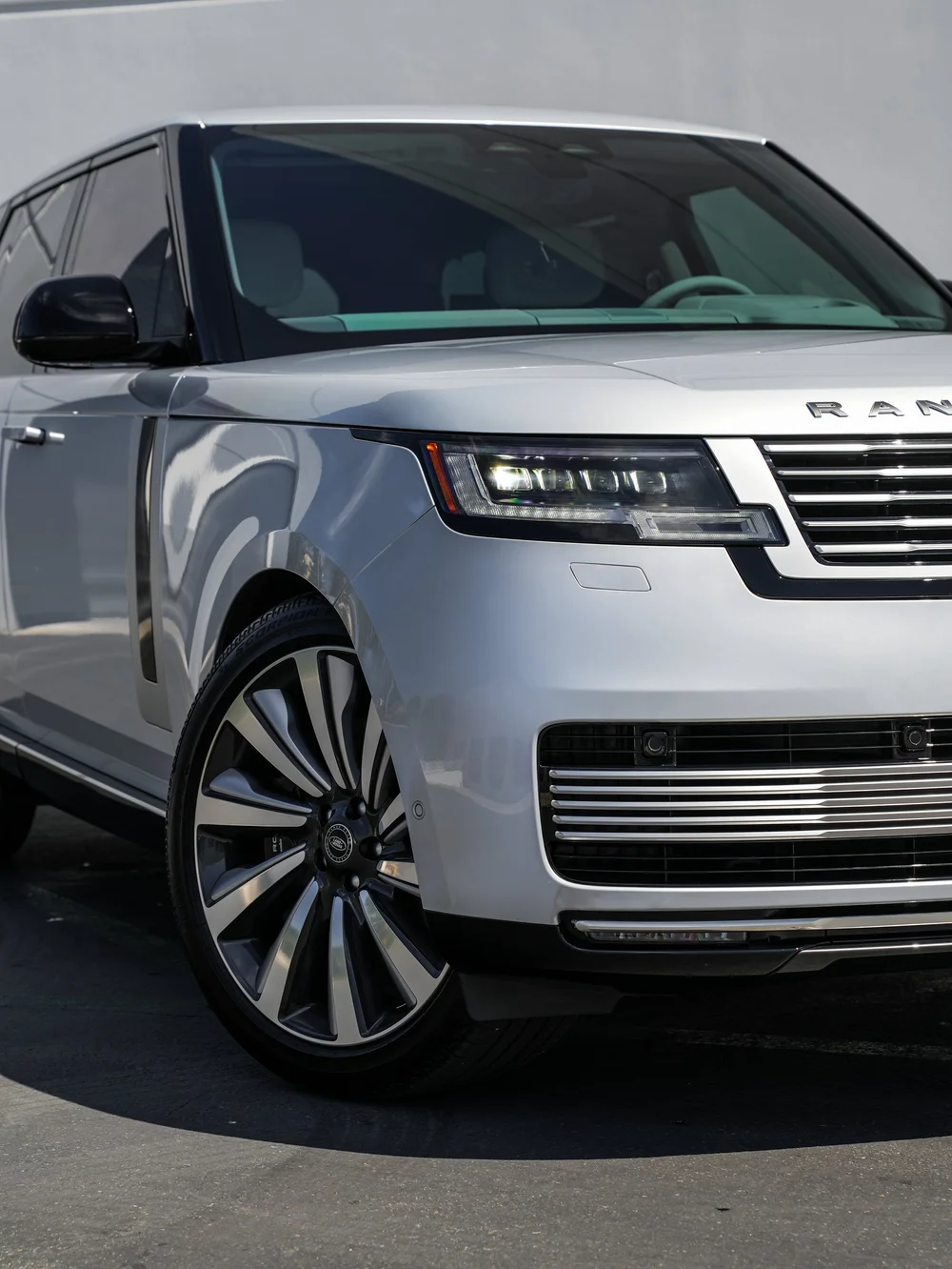 Front-corner detail of the silver Range Rover SV showing a headlamp, grille and multi-spoke wheel.