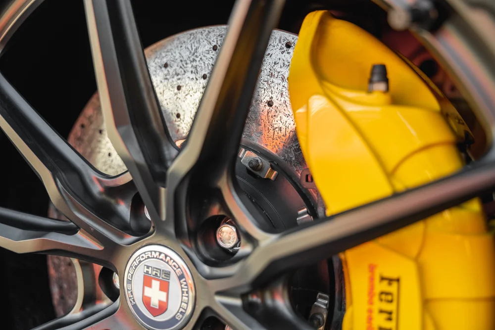 Close-up through the Ferrari SF90 black wheel spokes showing the perforated brake disc and yellow caliper