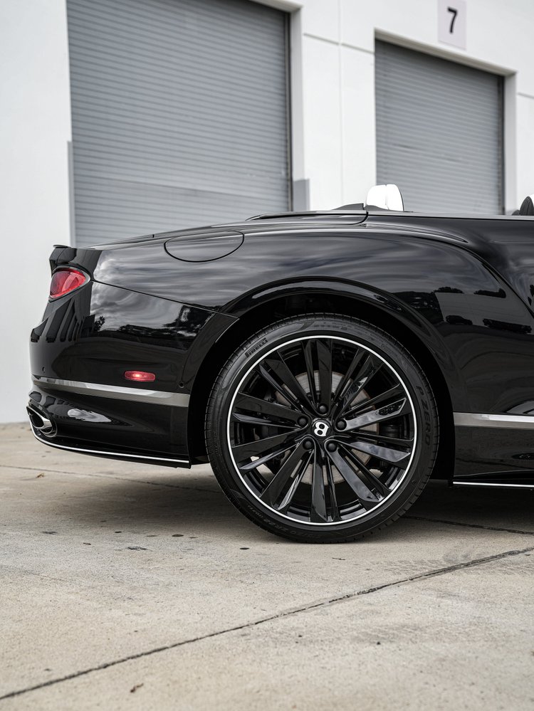 Bentley Continental GTC rear wheel, reflective black quarter panel, fuel door and oval taillamp edge.