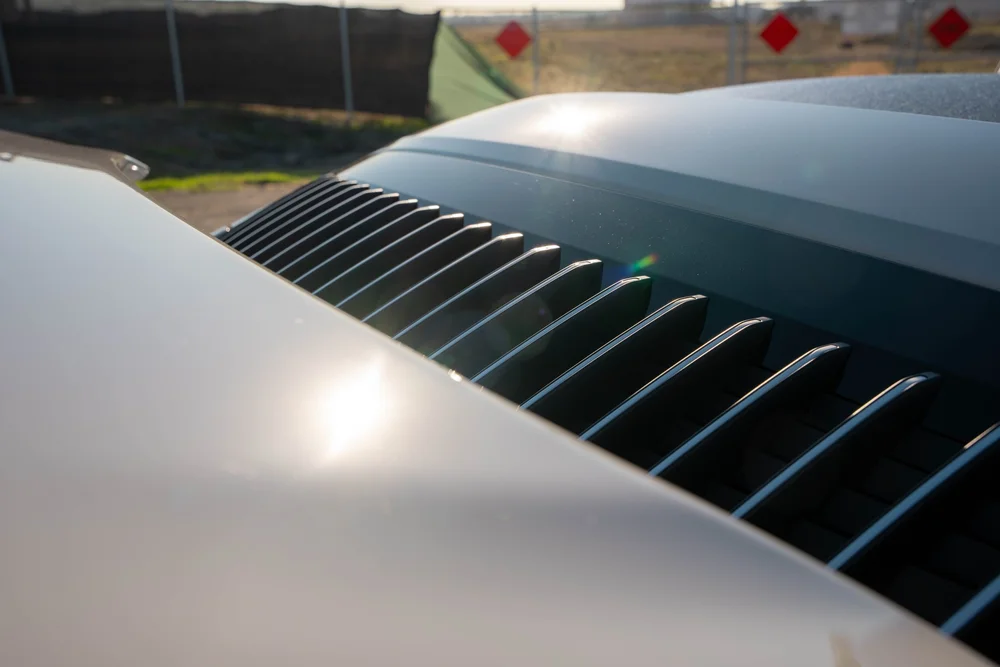 Chalk Porsche 911 Turbo S, raised rear spoiler and dark vent slats in sunlight