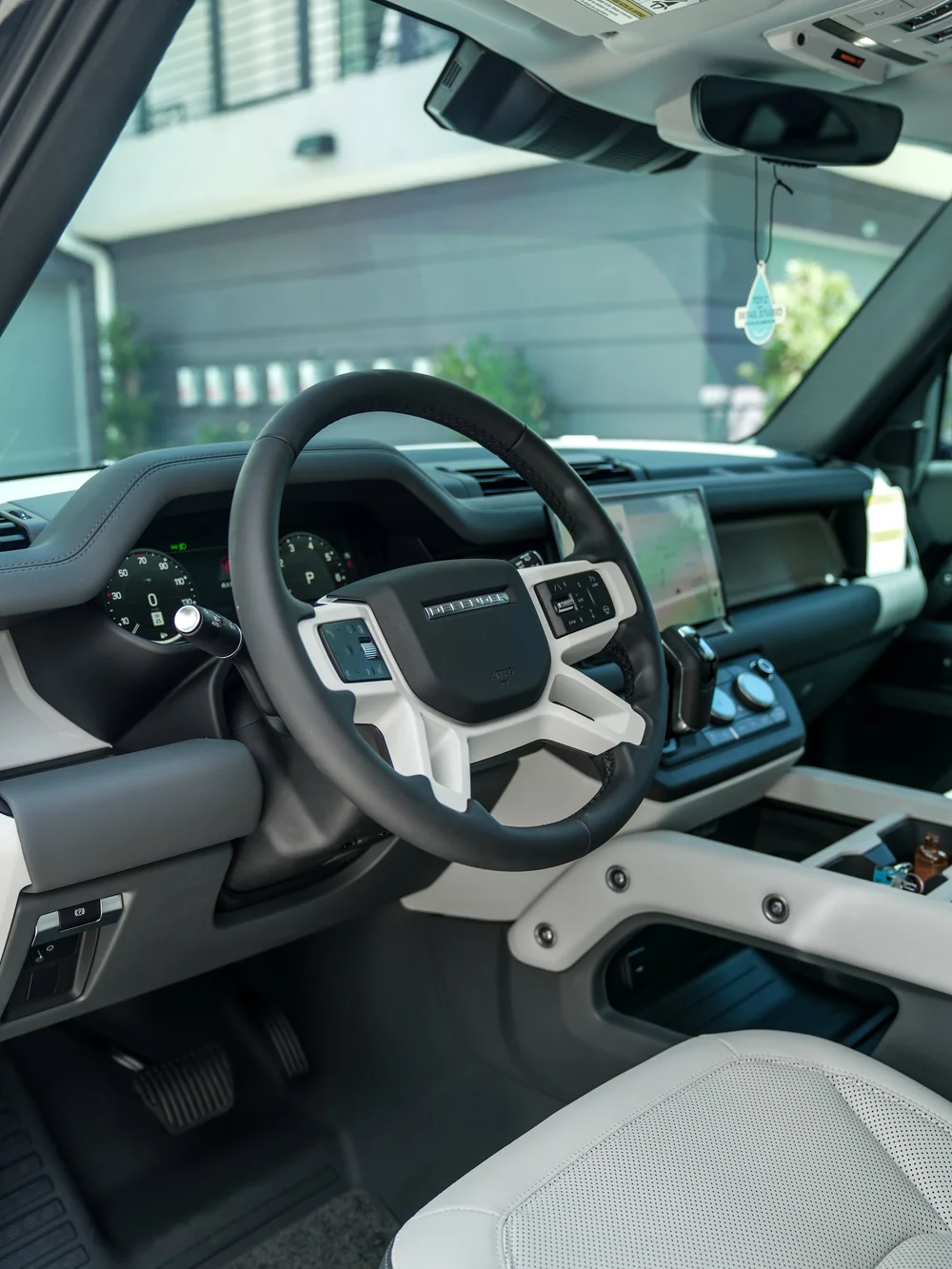 Light-and-dark Defender cabin through an open front door, with a DEFENDER steering wheel, instrument display, center map screen and light seat corner