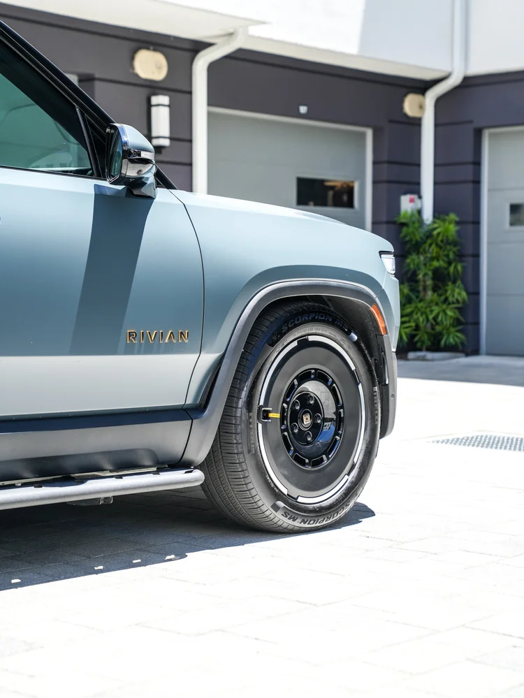 Rivian R1T front-side detail showing the satin door and fender, Rivian lettering, side mirror, front wheel and side step.