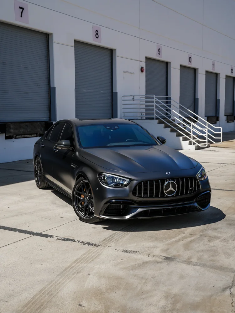 Alternate contrast version of the same right-facing front three-quarter composition of the Mercedes-AMG E 63 S, showing the complete dark body, grille, wheels and yellow-gold calipers.