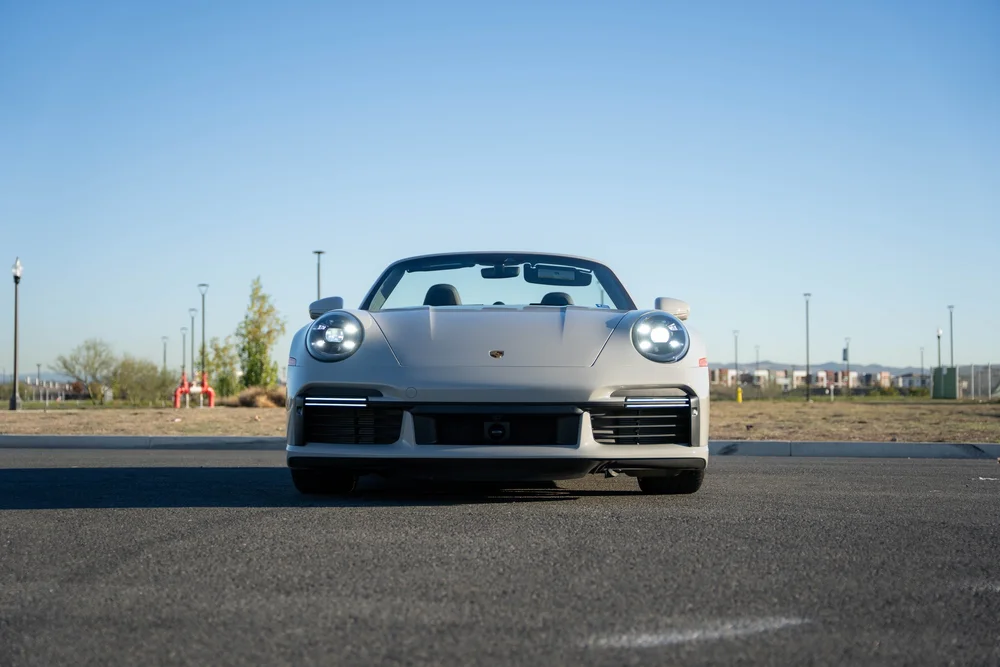 Chalk Porsche 911 Turbo S, complete low straight-front view with headlights illuminated