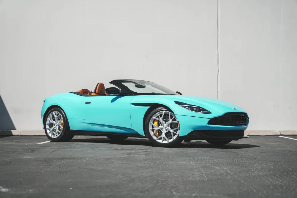 Miami Blue Aston Martin DB11 with roof lowered in a complete front three-quarter view, silver wheels and yellow brake calipers